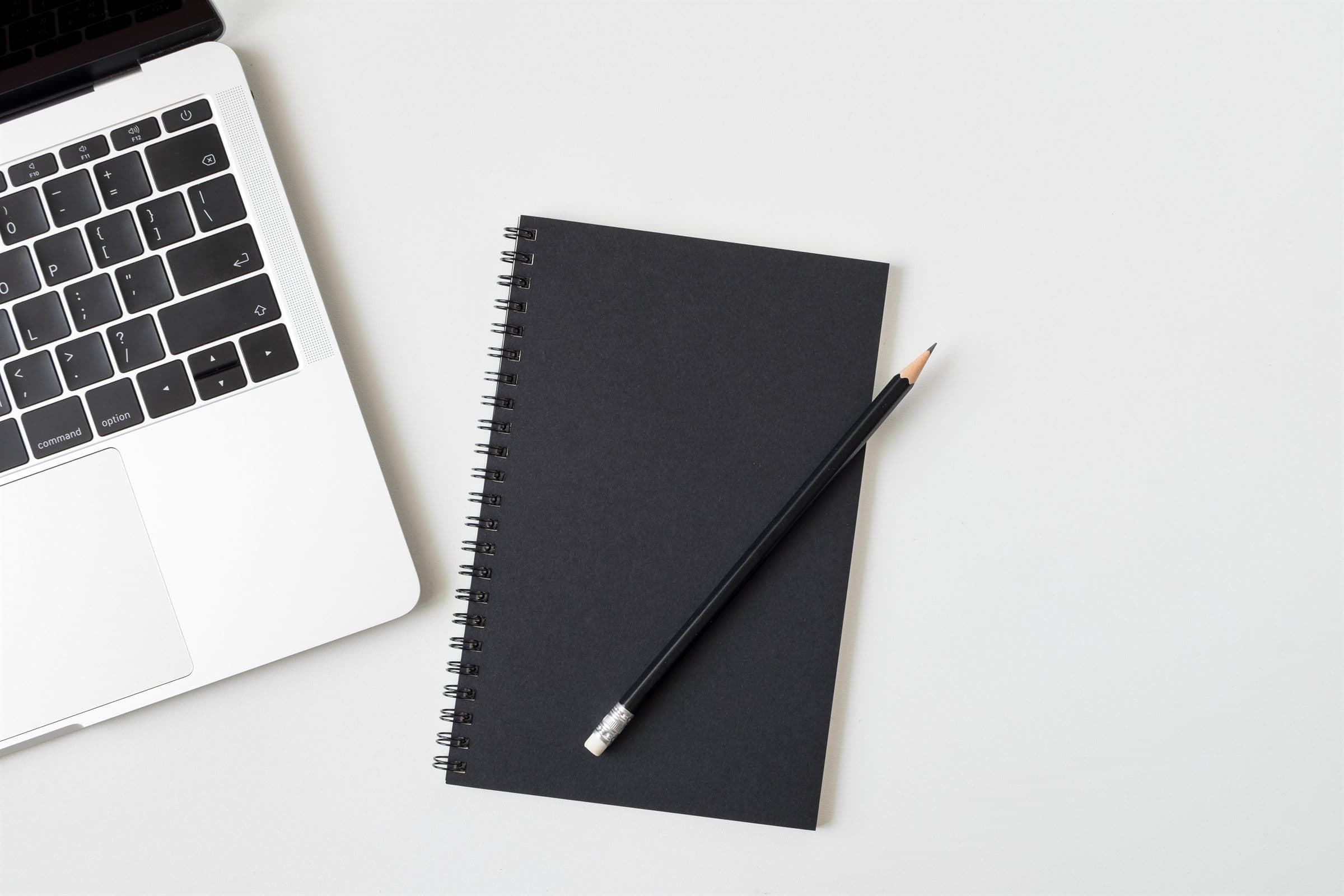 Mold Assessment & Remediation Protocols — A closed black notebook and a sharpened pencil resting on a plain white desk beside an open laptop (illustrative)
