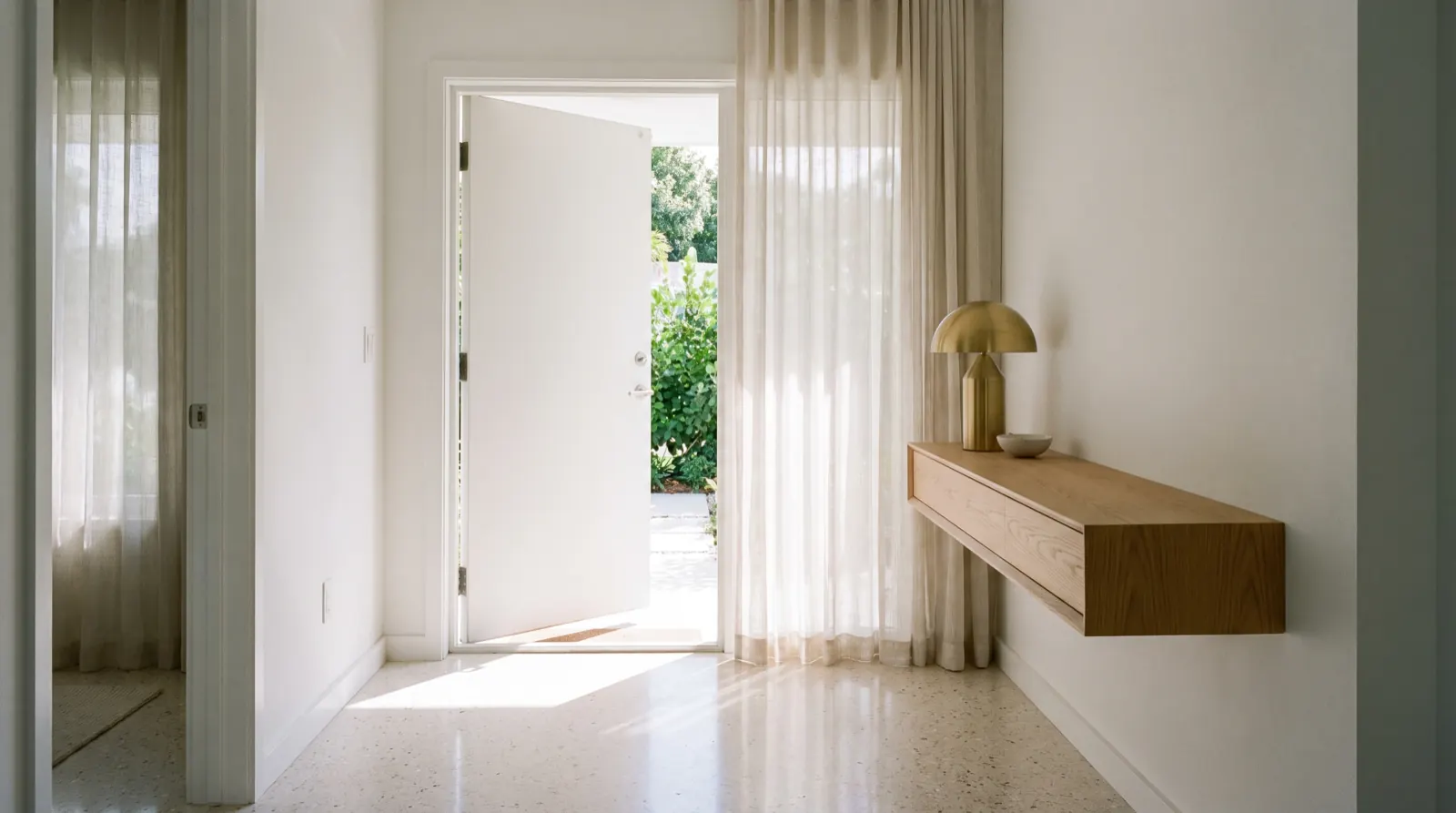 An entry hallway with the front door open to soft daylight and a brass lamp on a floating console (illustrative)