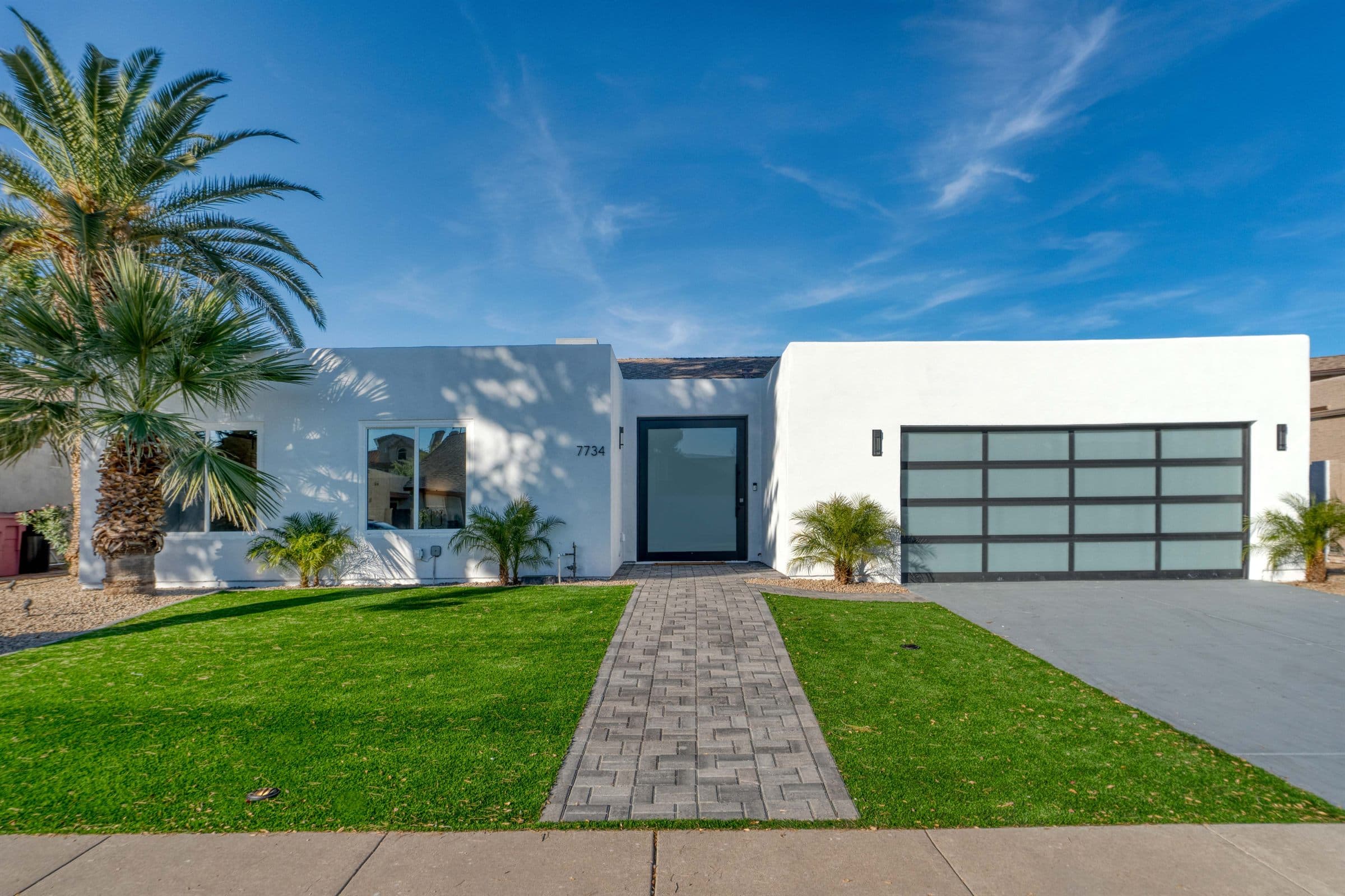 Real Estate Mold Inspections — A single-storey white stucco home with a paved front walk, clipped lawn, and palms under a clear blue sky (illustrative)